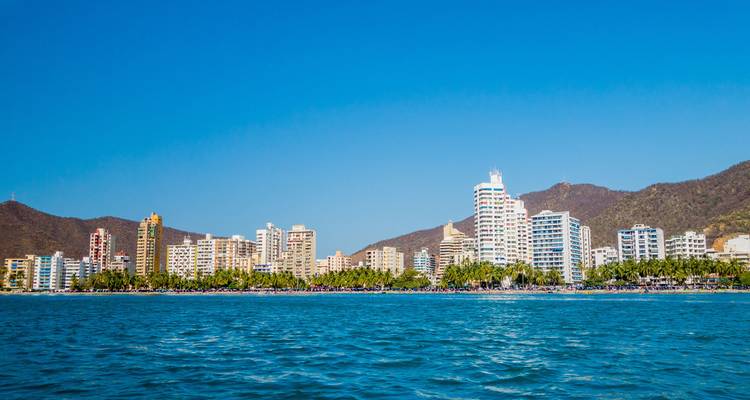 Seafront skyline of Santa Marta with modern high-rise hotels and blue waters backed by dusty brown hills.