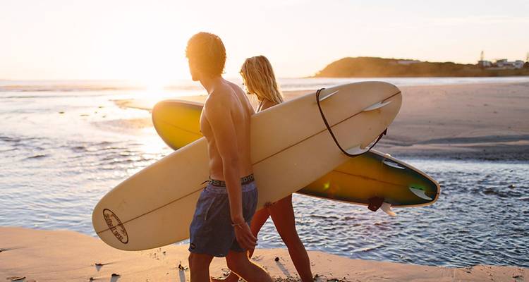 Twee surfers lopen langs het strand met boards in de gloeinde zonsopgang.