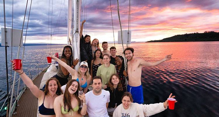 Grupo sonriente de viajeros celebrando en un yate al atardecer sobre aguas tranquilas del lago.