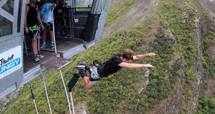 Person beim Bungee-Sprung von einer Plattform über eine bewaldete Schlucht.