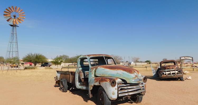 Camiones vintage oxidados yacen abandonados en un asentamiento desértico polvoriento bajo un cielo azul despejado