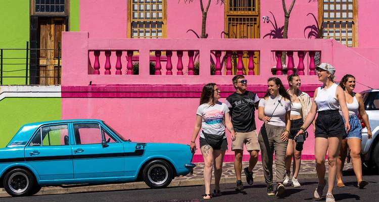 Groupe marchant devant des maisons colorées dans un quartier urbain animé, probablement Bo-Kaap, Le Cap.