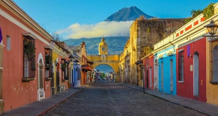 Calle colonial colorida de Antigua enmarcada por el Arco de Santa Catalina y el volcán que se cierne sobre ella.
