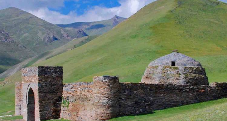 Stone caravanserai ruins in a hilly landscape under a bright sky.