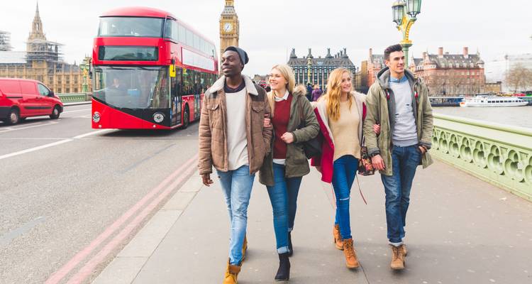 Gruppe von Menschen, die eine Brücke in einer Stadt mit einem roten Bus überqueren.