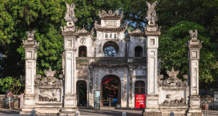 Entrée d'un temple ancien avec des sculptures complexes et des arbres alentour.