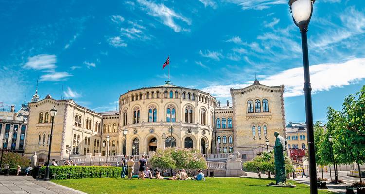 Parlamentsgebäude mit Touristen auf einer grasbewachsenen Wiese an einem sonnigen Tag.