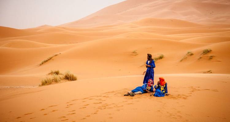 Tres personas con vestimenta azul sentadas en dunas de arena.