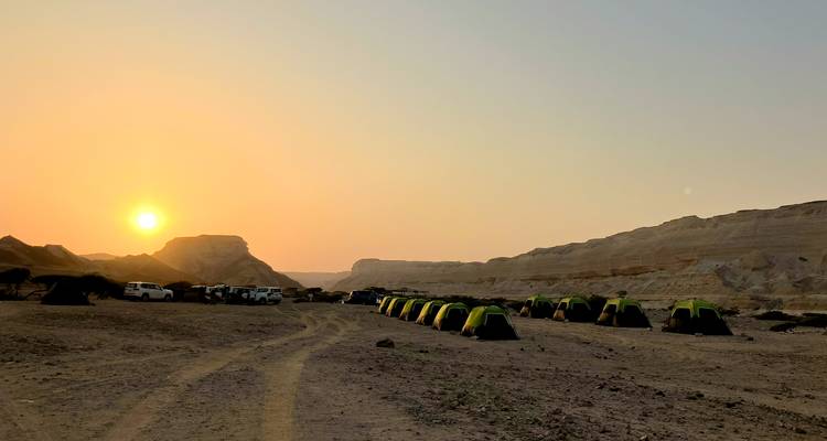 Reihe grüner Zelte, die bei Sonnenaufgang auf einer kahlen Wüstenebene mit nahegelegenen 4x4-Fahrzeugen aufgestellt sind