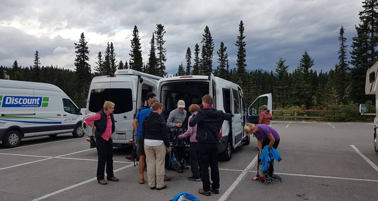Menschen versammelten sich um einen Transporter auf einem Parkplatz mit bewaldeter Umgebung.