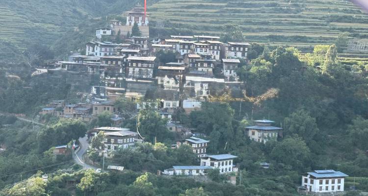 Des flancs de collines en terrasses parsemés de maisons bhoutanaises traditionnelles se regroupent autour d'un temple au sommet d'une colline.