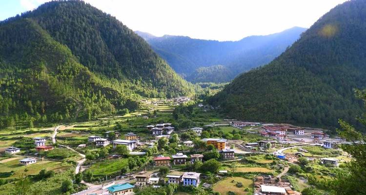 Un village rural de vallée bhoutanaise niché entre deux montagnes densément boisées.