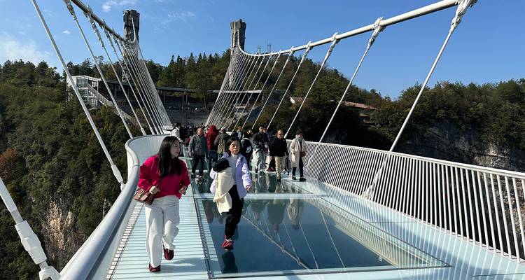 Personas caminando sobre un puente de suelo de cristal en las montañas.