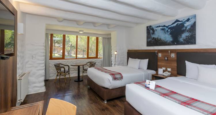 Modern hotel room with two double beds, wood floors, mountain artwork and a large window to greenery.