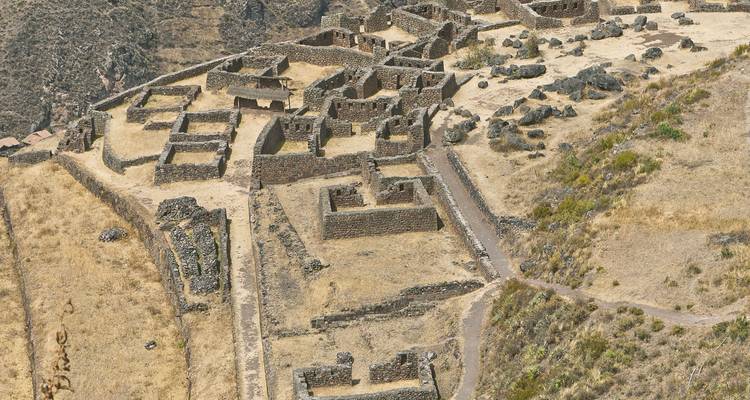Aerial view of Pisac archaeological ruins laid out on a dry mountain slope.