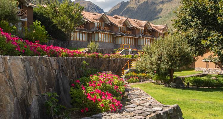Charming mountain resort lined with bright pink flowers and backed by steep peaks under sun.