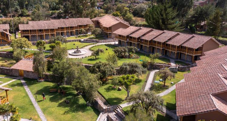 Drone view of a sprawling countryside lodge complex with central fountain and green lawns.