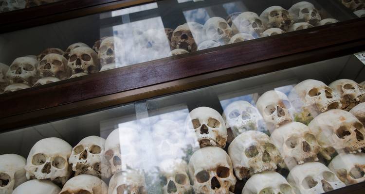 Pilas de cráneos humanos colocadas detrás de paneles de vidrio dentro de una vitrina conmemorativa, con reflejos del cielo.