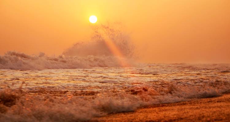 Sunset over the ocean waves creating a warm, orange-hued sky.