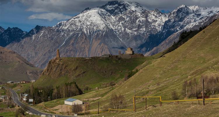 Las montañas del Cáucaso cubiertas de nieve elevándose detrás de un valle verde e iglesia antigua cerca de Stepantsminda.