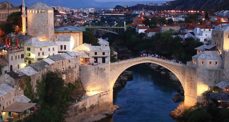 Las luces vespertinas brillan en el histórico puente de piedra de Mostar que se arquea sobre el río Neretva de color esmeralda.