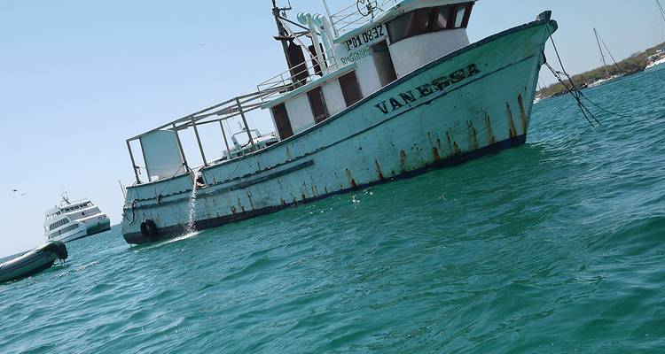 Ancien bateau de croisière blanc flottant sur une mer d'eau turquoise avec de légères taches de rouille le long de sa coque.
