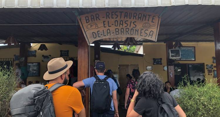 Des routards entrant dans un bar-restaurant rustique avec une enseigne en bois peinte à la main en espagnol.