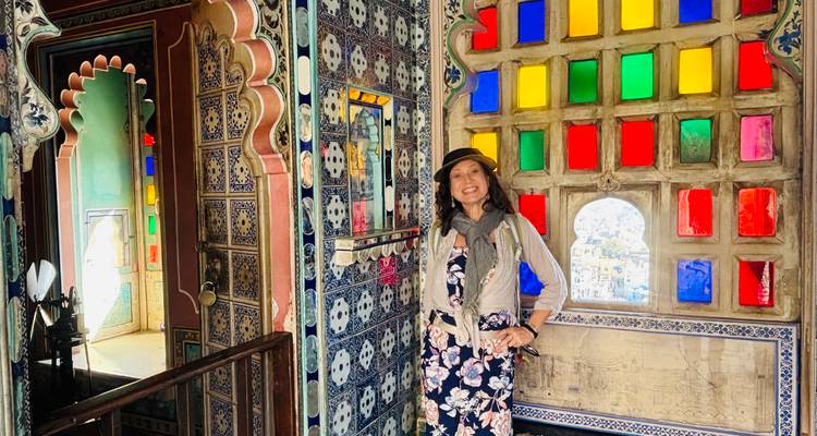 Reisender posiert neben bunten Glasfenstern und kunstvollen blauen Kachelarbeiten im Udaipur-Palast.