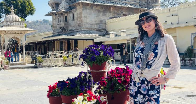 Un voyageur souriant se tient à côté de pots de fleurs colorés dans la cour ensoleillée d'un complexe de temple hindou en pierre.