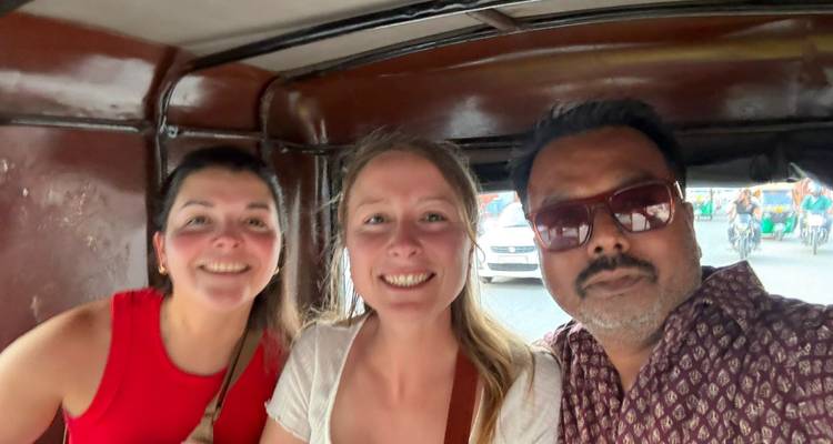 Selfie de deux voyageuses et d'un chauffeur souriant à l'intérieur d'un tuk-tuk en mouvement.