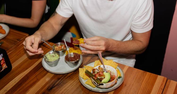 El comensal se prepara para disfrutar de tortillas crujientes con guacamole y salsa en una mesa de madera.