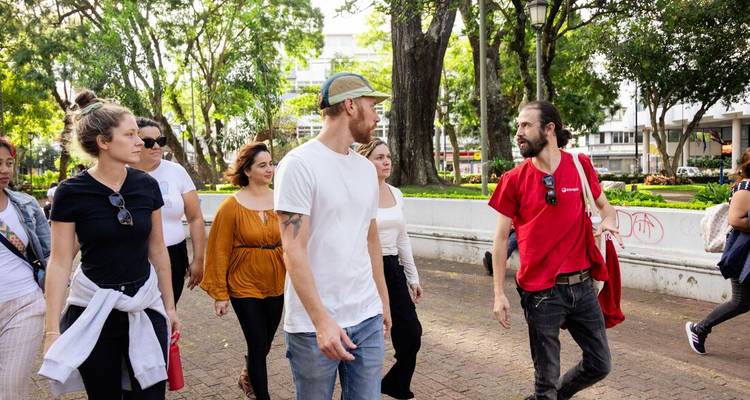 Un grupo de turismo camina por un parque urbano lleno de vegetación escuchando a su guía local.