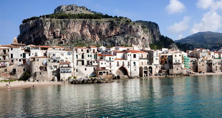 Encantador pueblito junto al mar con casitas de colores pastel agrupadas contra un acantilado rocoso, reflejadas en aguas turquesas tranquilas.