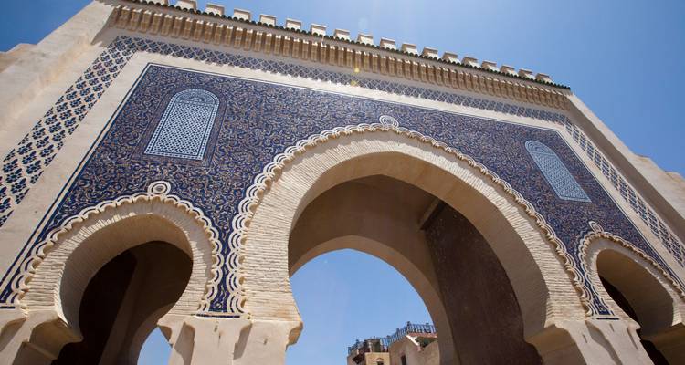 Toma en ángulo bajo de la puerta Bab Bou Jeloud en Fez con intrincados azulejos de mosaico azul contra un cielo despejado.