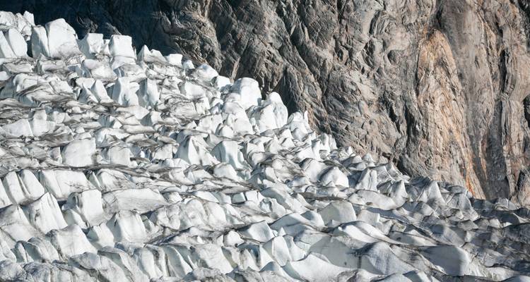 Close view of glacier ice formations against rocky mountain.