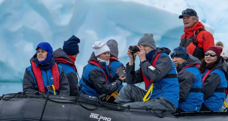 Ein Team von ausgerüsteten Entdeckern in einem schwarzen Zodiac fotografiert massive antarktische Eisformationen aus nächster Nähe.