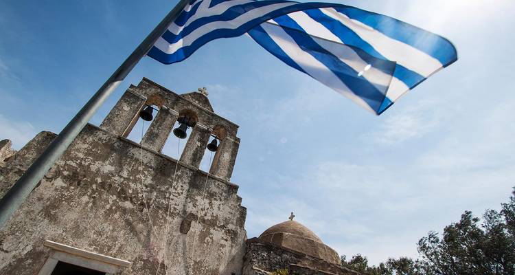 Griekse vlag wappert naast een oude klokkentoren onder een heldere hemel.