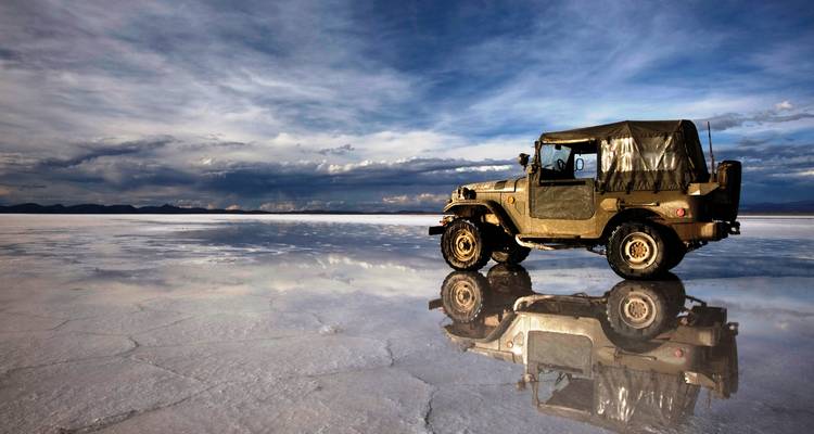 Un véhicule 4x4 sur un désert de sel réfléchissant sous un ciel dramatique.