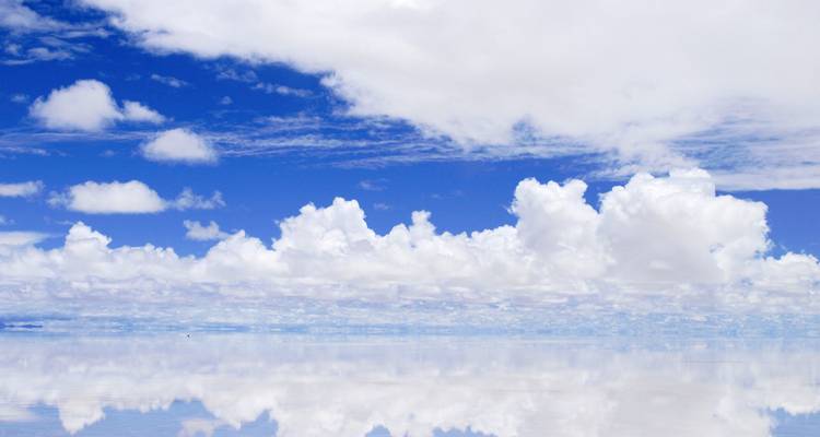 Ciel bleu dégagé et nuages cotonneux se reflétant sur un lac salé calme.
