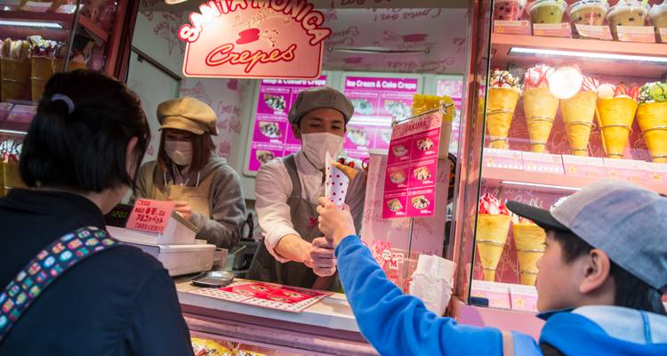 Un vendedor enmascarado entrega crepes recién hechos a los clientes en un puesto rosa de Harajuku.