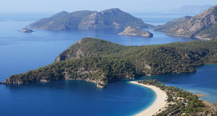 Vista aérea de las penínsulas cubiertas de pinos y la playa de arena curva de Ölüdeniz contra las aguas azul profundo del Mediterráneo.