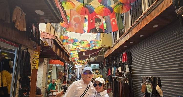 Una pareja de pie bajo sombrillas coloridas con banderas turcas en una calle de mercado estrecha.