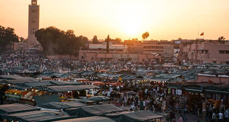 Busy market scene with tents and a tall tower during sunset.