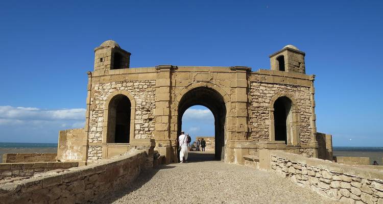 Stone sea-front bastion archway at Essaouira with visitors strolling toward the ocean horizon.