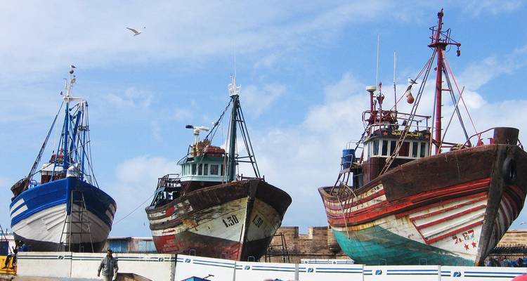 Row of colourful wooden fishing trawlers hauled onto dry dock under a blue sky.