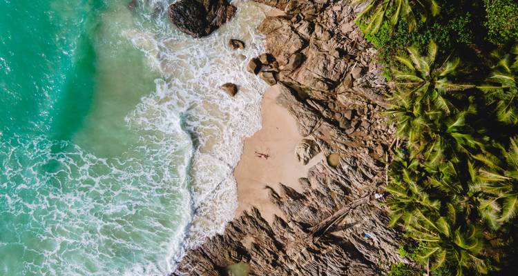 Vue aérienne d'une plage isolée avec des eaux turquoise et une végétation luxuriante.