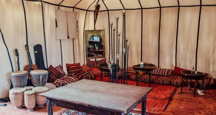 Gemütliches Berber-Zeltinneres mit Kissen, Trommeln und Instrumenten um einen niedrigen Tisch.