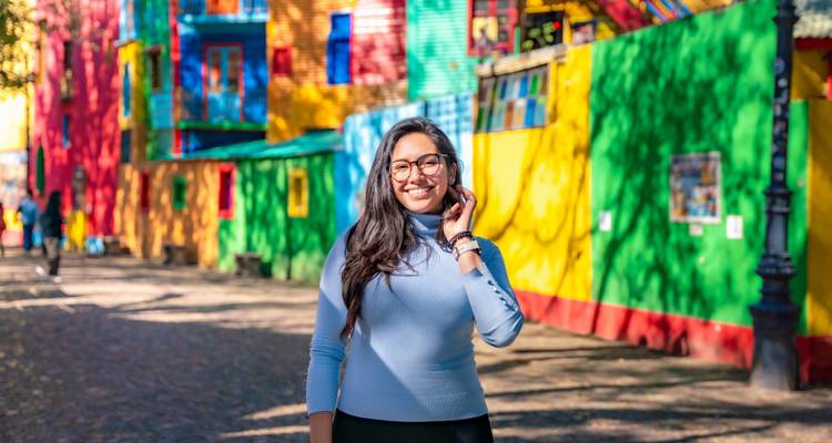Jeune femme souriante devant des bâtiments colorés.