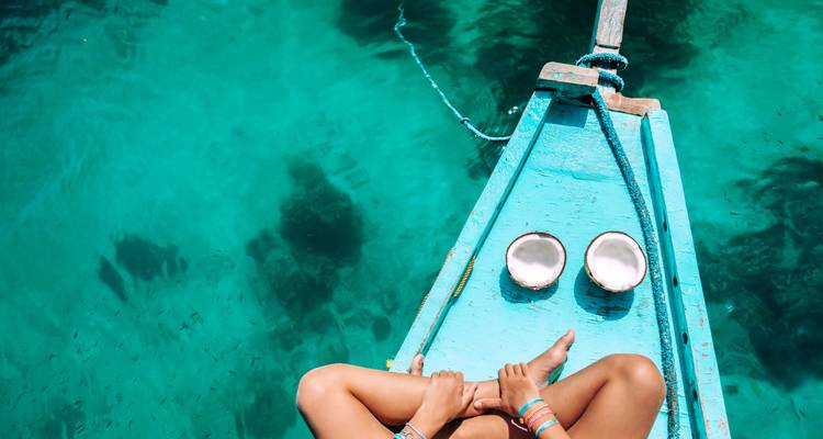 Person, die auf der Vorderseite eines Bootes über klarem Wasser sitzt