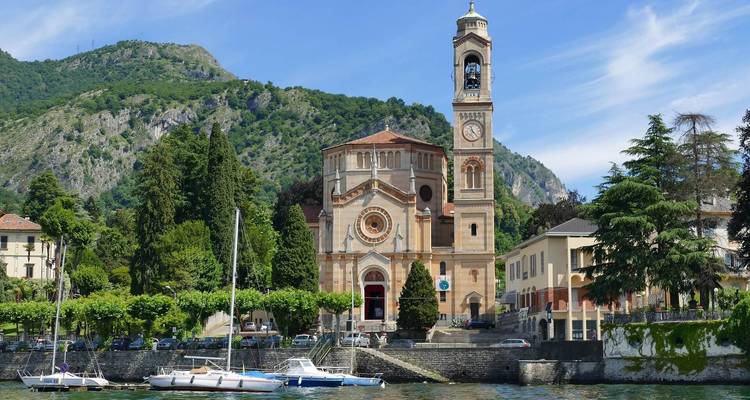 Église au bord d'un lac avec montagnes et bateaux amarrés.